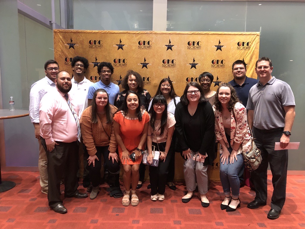 A group of students gather in front of an orange backdrop